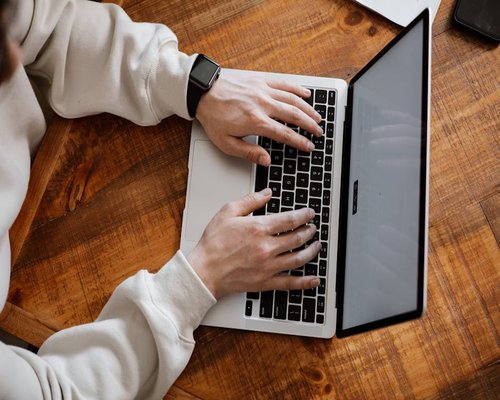 Person adjusting laptop screen angle at a wooden desk
